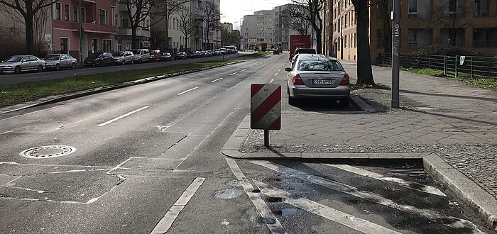 Bestandsituation Bereich Radwegquerung zweispurige Fahrbahn mit längsparkenden Autos im Parkstreifen, Gehweg und Bebauung