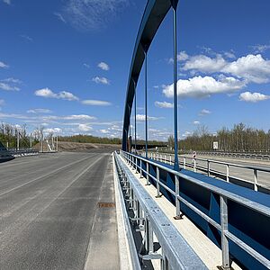 Blick auf das Brückenbauwerk, blaue Bogenbrückenkonstruktion, Fahrbahn mit Entwässerungs-Einlauf