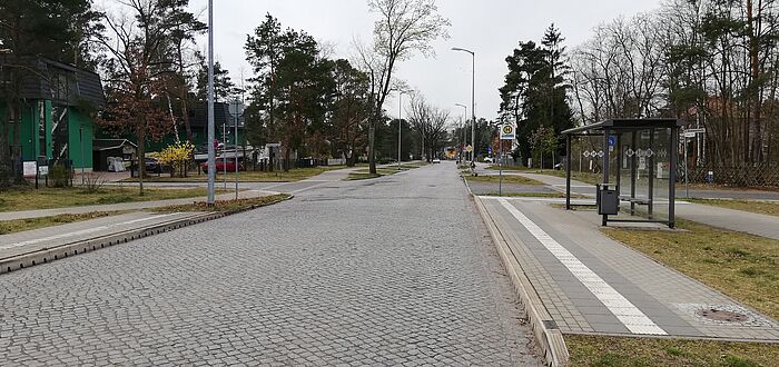 Blick auf Kreuzungsbereich, rechts Bushaltestelle, angrenzender Grünstreifen und Gehweg, dahinter lockere Bebauung