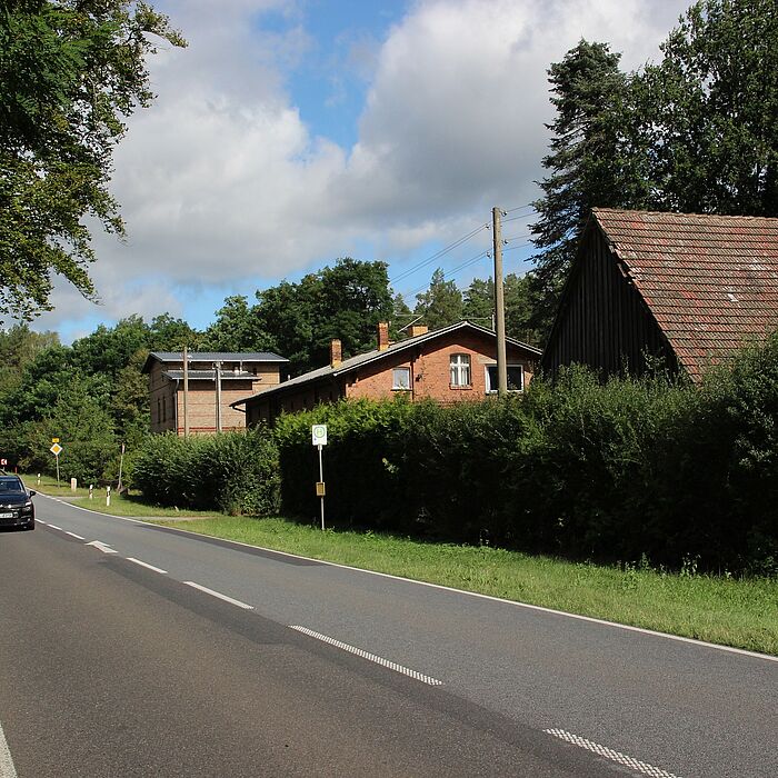 Streckenbereich mit Baumbestand links, rechts Bebauung und ein Bushaltestellenschild