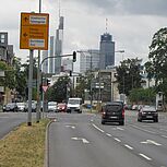 mehrspurrige Kreuzung mit Abbiegestreifen und Lichtsignalanlage, zahlreiche Fahrzeuge, im Hintergrund Skyline Frankfurt am Main