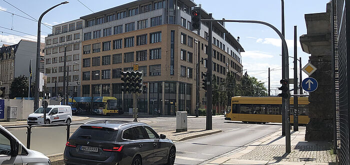 Fahrzeuge stehen vor roter Signalanlage, zwei Straßenbahnen überfahren in gegensätzlicher Richtung die Kreuzung