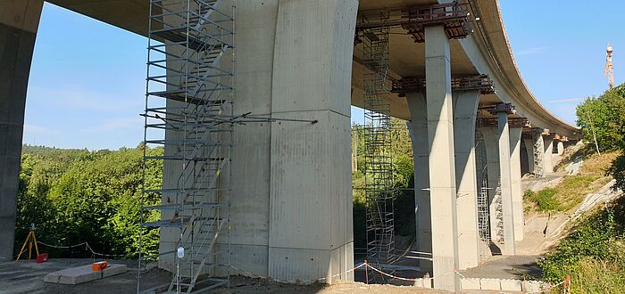 Blick auf die Konstruktion der Brücke von unten und auf die Stützen, Blick auf die Baustelle mit Gerüsten und Kran im Hintergrund