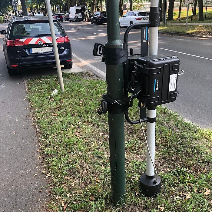 Erfassungsgerät an Pfosten neben Fahrbahn, im Hintergrund Fahrzeug