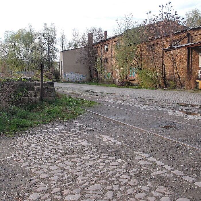 alte Pflasterstraße mit Gleisen, im Hintergrund verfallene Gebäude