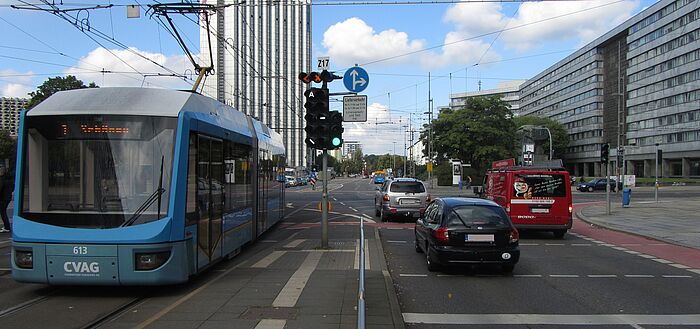Kreuzungsbereich, Straßenbahn und Fahrzeuge fahren parallel über die Kreuzung, Gebäude im Hintergrund