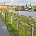 links Fahrradweg mit Radfahrer, Absperrung zum Neustädter Hafen, Hafen mit Schiff im Hintergrund
