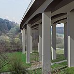 Blick auf die geplante Konstruktion der Brücke von unten und auf die Stützen, darunter befindlicher Weg mit Personen