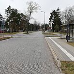 Blick auf Kreuzungsbereich, rechts Bushaltestelle, angrenzender Grünstreifen und Gehweg, dahinter lockere Bebauung