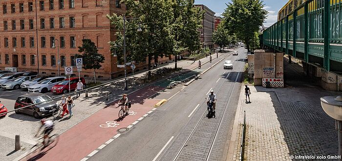 Blick auf die Straße mit rotem Radfahrstreifen, Radfahrer und Pkw, U-Bahn-Viadukt rechts, Bebauung