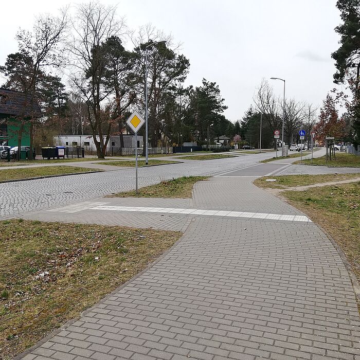 Verschwenk des Gehwegs an die Fahrbahn mit Blindenleitstreifen im Gehweg zum Überqueren der Straße, dahinter Straßeneinmündung, Bebauung